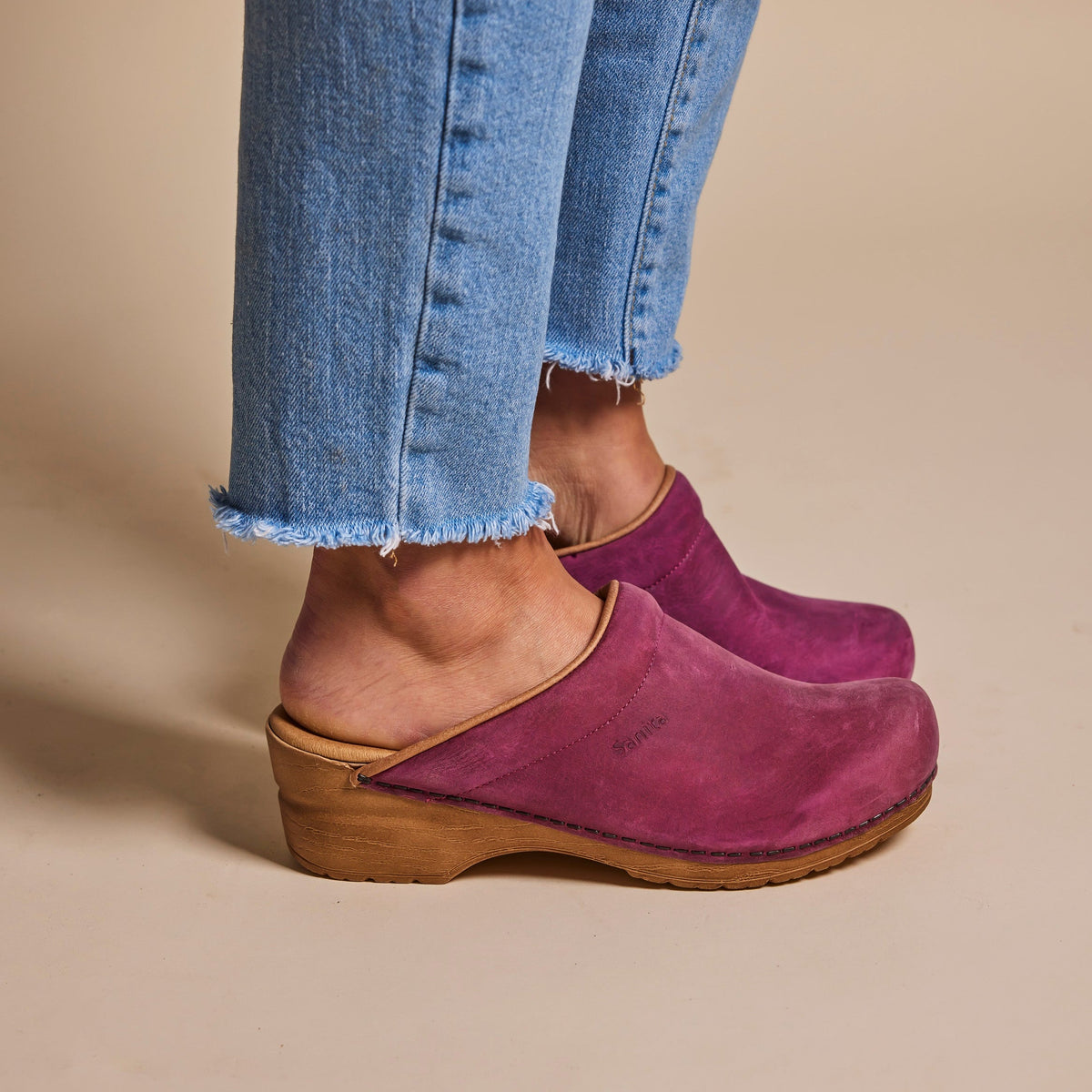 Fuchsia colored clogs worn with blue jeans on a beige background